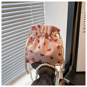 Detailed view of pink corduroy bucket bag with strawberry prints and pearl chain strap