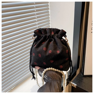 Detail of black corduroy bucket bag with strawberry print and white pearl handle strap