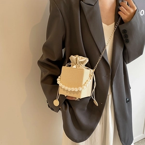 Chic beige bucket bag with pearl handle, gold chain strap, and drawstring closure for women