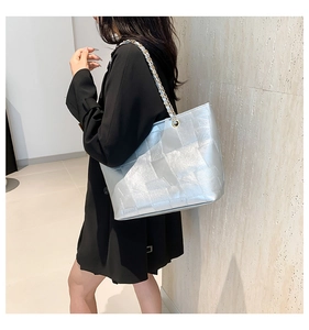 Model showing a large silver metallic tote bag with geometric patchwork and gold chain strap