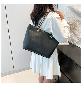 Detail of black geometric leather tote bag with gold chain strap worn by a model