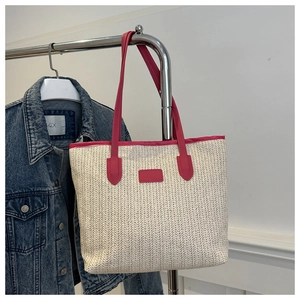 Détail d'un cabas en paille tressée avec garniture et anses en cuir rose sur un présentoir