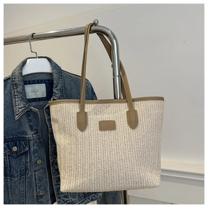 Détail du sac cabas en paille tressée avec anses en cuir kaki et coutures contrastées