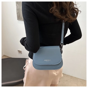 Side view of a Morandi blue leather crossbody bag worn by a model in a minimalist room