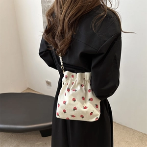 White corduroy bucket bag with strawberry print and pearl chain shown on model