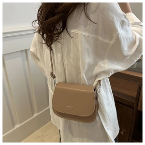 Detailed back view of a khaki saddle bag with silver lettering on white linen shirt