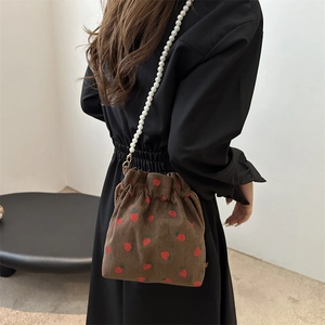 Brown corduroy bucket bag with strawberry print and pearl strap worn by a model