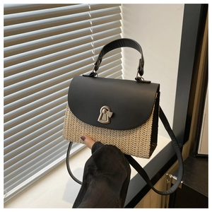 Detail of hand-held straw woven crossbody bag with black leather flap and gold metal clasp