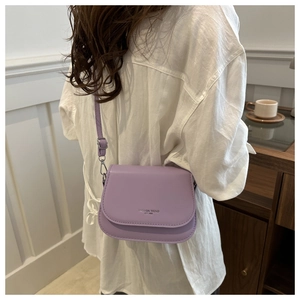 Model wearing a lilac crossbody bag with silver lettering on a clean home background
