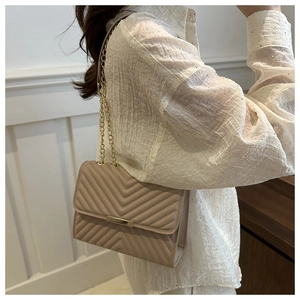 Detail of beige V-quilted crossbody bag with gold chain strap shown on model's shoulder