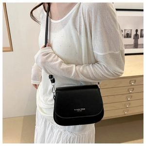 Close-up of black crossbody bag with adjustable strap worn by model in a modern interior