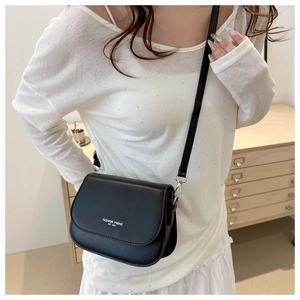 Close-up of black matte leather saddle bag with fashion trend lettering on white background