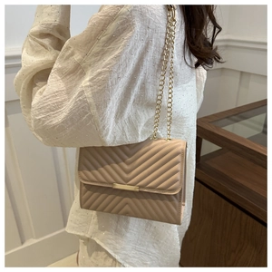 Beige quilted shoulder bag with V-shaped stitching and gold chain strap on model