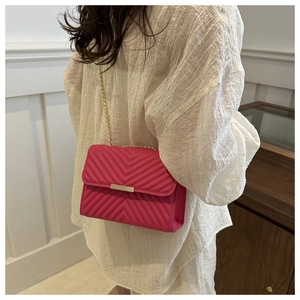 Detail of rose red quilted crossbody bag with golden chain strap and metallic buckle