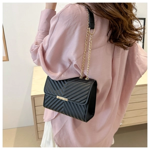 Detail of black quilted leather shoulder bag with gold chain and metal bar lock closure