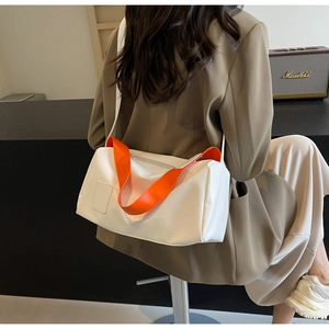 Side view of minimalist white pillow bag with vibrant orange wide strap on a model