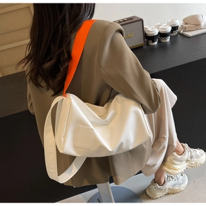 Detail of white nylon tote bag with bold orange shoulder strap shown on a model