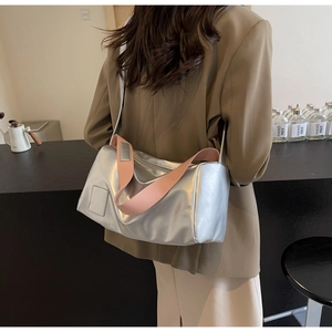 Silver rectangle shoulder bag with pink strap detail worn by model in a modern room