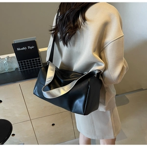 Minimalist black cylinder tote bag with stylish wide silver shoulder strap on a model