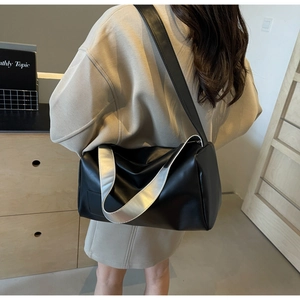 Detail of black cylindrical tote bag with silver handle worn by a model in interior setting
