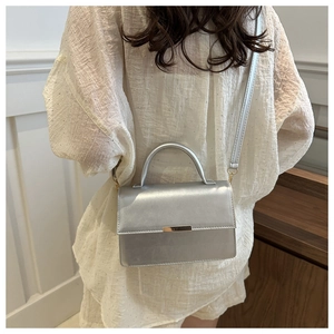 Silver metallic crossbody bag shown on model with a sleek envelope flap and metal buckle