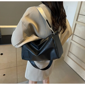 Detail view of the black minimalist cylinder bag with a wide metallic silver shoulder strap
