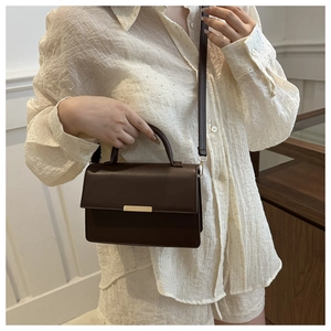 Detail of dark brown leather crossbody bag with gold metal clasp on elegant model