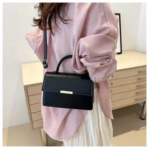Detail of a minimalist black leather square bag with a gold buckle worn as a crossbody