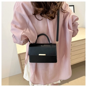 Detailweergave van een zwarte leren crossbodytas met gouden metalen sluiting op een model