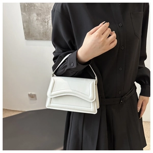 White glossy leather handbag with wavy edge detail shown on a black dress background