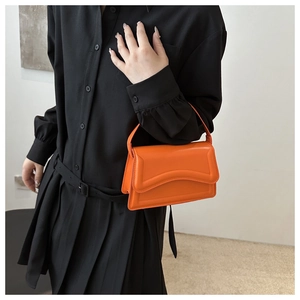Detail of bright orange small shoulder bag with wavy flap design on black clothing