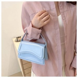 Close-up of light blue glossy leather shoulder bag with unique streamlined flap design