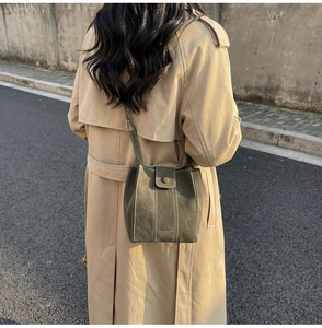 Close-up of matte dark green bucket bag with white contrast stitching and adjustable strap
