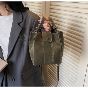 Detail of dark green bucket bag with white contrast stitching and gold logo