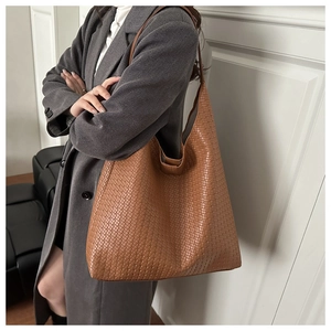 Close-up of a large warm brown woven leather tote bag worn with a grey wool coat