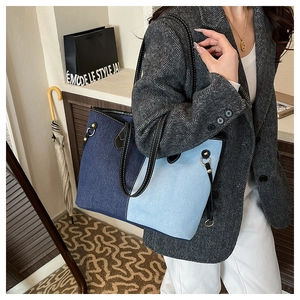 Detail view of large denim tote bag featuring contrast patchwork and a gold metal ring