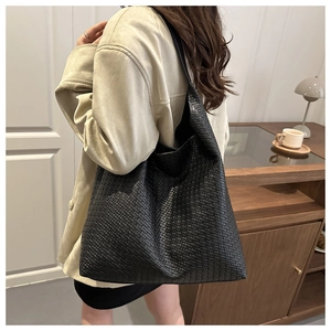 Large black woven tote bag shown on model's shoulder for size and styling reference