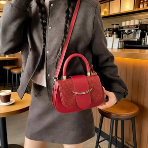 Detail of red leather crossbody bag featuring woven texture and gold curved metal accent
