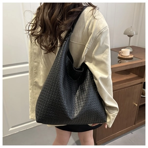 Détail d'un sac à bandoulière tressé noir montrant une texture fine et un style hobo