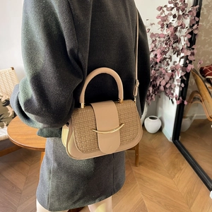Close-up of beige handbag featuring textured patchwork and a golden crescent metal buckle