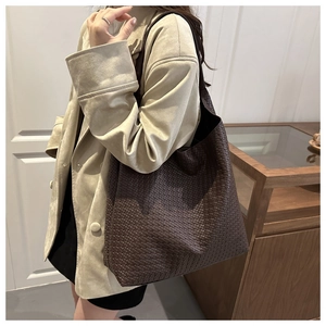 Detail view of a large dark brown woven leather tote bag shown on a shoulder