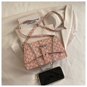 Detail view of pink crossbody bag with M-letter print and silver chain strap on white blazer