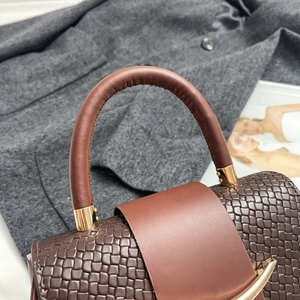 Macro detail of dark brown woven leather handbag with gold hardware and smooth handle