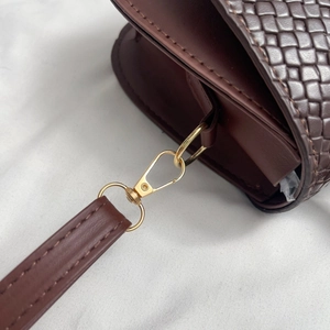 Close-up of golden hardware clasp on brown woven texture crossbody bag detail
