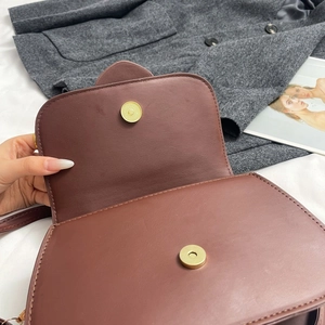 Detail view of brown leather bag showing gold magnetic buckle closures on flap