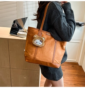 Detail of tan suede tote bag with cute plush charm showing shoulder carry style
