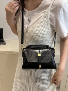Elegant black glossy small square bag with gold buckle shown on a model in a minimalist setting