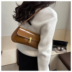 Détail d'un sac porté épaule en cuir verni marron avec boucle en métal doré sur modèle