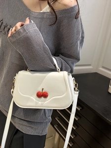 White leather shoulder bag featuring decorative red cherry charms and a top handle strap