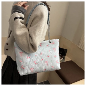 Detail of light blue corduroy tote bag featuring pink floral bow prints and chain strap